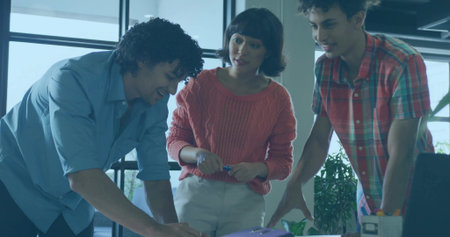 Holding pen, woman in coral sweater reviewing documents with two men at office desk, purple binder....