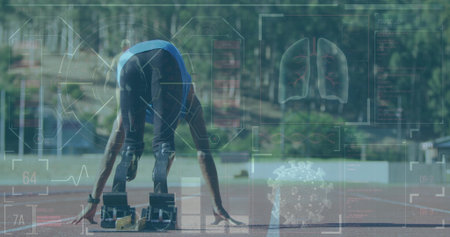 Preparing teenage sprinter in blocks at track, sporting blue top, spikes and wristband. Athlete,...