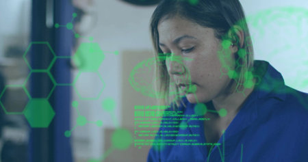 Concentrating female technician in blue coveralls examining screen at lab with green AR hexagons. Holographic, interface, display, futuristic, geometric, overlay, laboratoryの写真素材