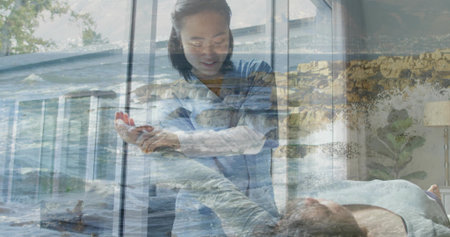Leaning caregiver in light-blue scrubs holding and guiding patient's arm at bed, with ocean overlay. Nurse, assist, seascape, double-exposure, tranquil, coastal, interiorの写真素材