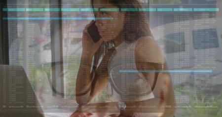 Woman in sleeveless top and wristwatch speaking on phone at desk by window, laptop, data overlay. Remote, workspace, daylight, foliage, interface, minimalist, modernの写真素材