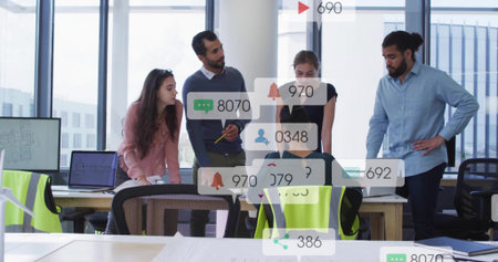 Reviewing five-person team in smart casual at table near windows with laptop hi-vis vests alerts. Collaboration, colleagues, analytics, data, openplan, daylight, urbanの写真素材