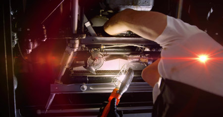 Leaning gloved mechanic in white shirt checking undercarriage with caged lamp red cable, copy space....