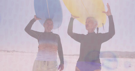 Standing couple wearing rash guards and swim bottoms carrying blue and yellow surfboards on beach....