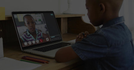 Sitting child in denim shirt watching live call at desk with laptop, pencils, paper, copy space....