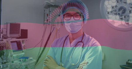 Standing clinician arms crossed wearing scrubs bouffant mask glasses in OR stethoscope  and  monitors. Operating, surgery, hospital, physician, anesthesia, screens, equipmentの写真素材