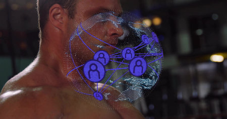 Turning shirtless man projecting holographic globe with user icons in dim gym interior. Athlete, physique, projection, network, connectivity, digital, visualizationの写真素材
