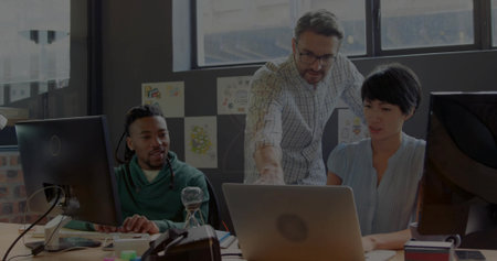 Pointing man in checkered shirt guiding team in light blouse, green hoodie at desk with laptop....