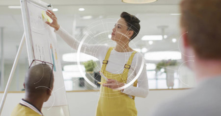 Placing sticky note presenter wearing yellow overalls reaching at flip chart in office, HUD overlay....