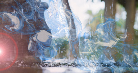 Floating glassy blue water swirls creating reflections on shallow pool near trees with lens flare. Translucent, abstract, reflective, bokeh, outdoor, woodland, dropletsの写真素材