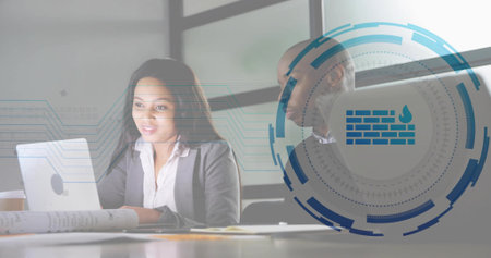 Collaborating woman in blazer using laptop at meeting table, with rolled plans. Teamwork,...