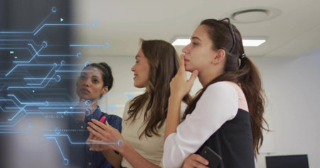 Reviewing three women wearing blouses at meeting room glass display with circuit overlay and phone....