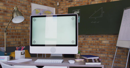 Displaying white all-in-one monitor with stand on desk in study, with keyboard, lamp, chalkboard. Computer, workspace, classroom, geometry, formula, pencils, notebooksの写真素材