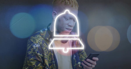 Holding smartphone, man wearing botanical jacket viewing neon bell alert in studio with bokeh. Portrait, fashion, pattern, notification, blue, amber, stageの写真素材