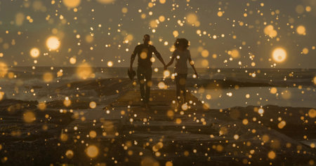 Walking couple holding hands on jetty at sunset, golden bokeh, man carrying cap, woman short dress. Silhouette, romance, dusk, pier, waves, backlit, bokehの写真素材