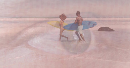 Walking couple carrying yellow, blue surfboards at shore in bikini and shorts, rock and eye overlay....