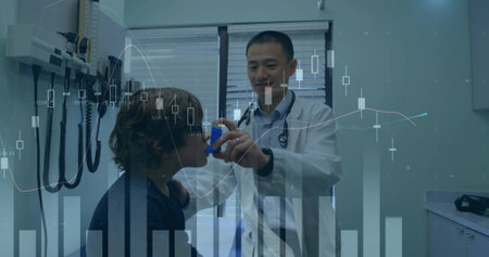 Administering doctor in white coat giving blue spacer to boy in exam room, financial charts overlay. Inhaler, pediatric, clinic, physician, medical, equipment, graphsの写真素材