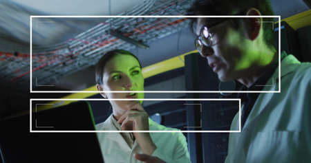 Discussing two lab coat engineers examining laptop in server room, showing yellow cable tray....