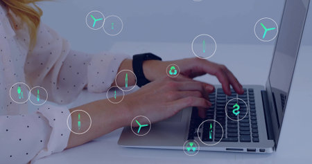 Typing woman wearing dotted blouse, black smartwatch at white desk on laptop, showing green icons. Keyboard, remote, workspace, sustainability, renewable, wind, recyclingの写真素材