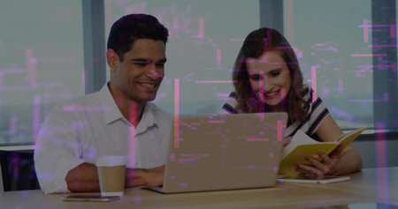 Working pair leaning over laptop at office, in white shirt and striped top, holding yellow notebook....