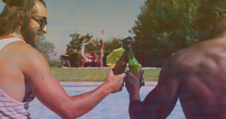 Clinking men in shades and swimsuits seated at pool edge, holding green bottles near picnic blanket. Outdoor, leisure, friends, backyard, lawn, sunny, glasswareの写真素材