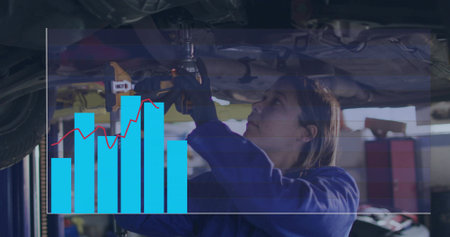 Tightening mechanic in blue coverall under raised vehicle at garage, using drill with chart overlay....