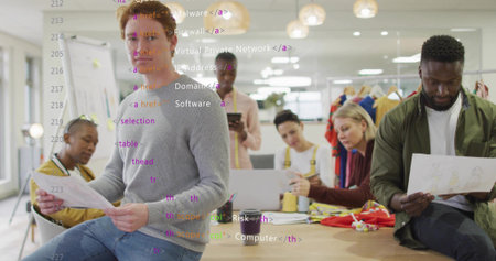 Discussing creative team reviewing printed sketches in design studio, with laptop, clothing rack....