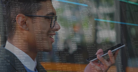 Speaking man in business attire holding smartphone near mouth at modern office, with code overlay. Professional, security, tech, glasses, suit, contemporary, reflectionsの写真素材