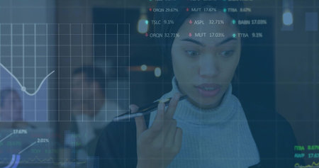 Studying woman in turtleneck and blazer holding pen in office, glass display with financial charts. Datadriven, analytics, collaboration, dashboard, corporate, boardroom, focusの写真素材