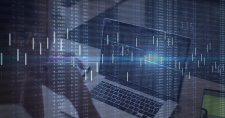 Showing laptop keys, screen at office desk, left figure wearing dark top holding phone, market data....