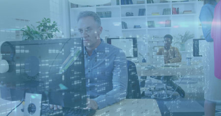 Typing man wearing button-up shirt at front desk in open-plan office, with monitors and reflections....