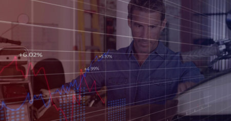 Man in blue denim shirt studying charts on monitor at home office, with suitcase and mic. Finance,...