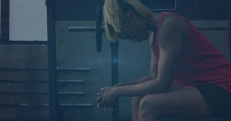 Sitting woman wearing sleeveless red top, shorts, hunching on bench near rack in gym, copy space. Solitary, athlete, training, weightlifting, powerrack, equipment, moodyの写真素材