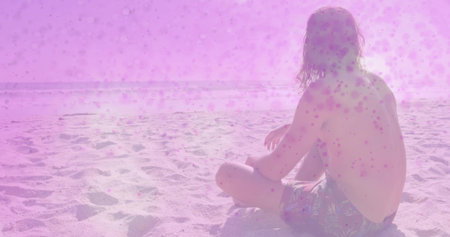 Sitting man watching pink sea glare at sandy beach with prints, patterned swim trunks, copy space. Coastal, horizon, backlit, solitude, contemplative, calm, minimalistの写真素材