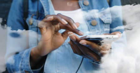 Tapping woman wearing denim jacket and white top at window, phone and earphone cable showing, nails. Hands, mobile, clouds, reflection, glass, urban, stylishの写真素材