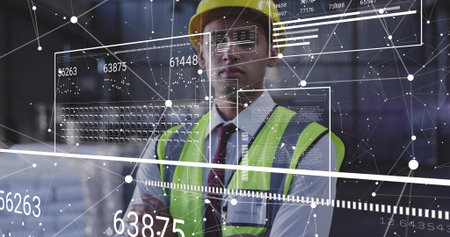 Checking site engineer viewing digital UI inside warehouse, yellow hard hat, lime vest, ID badge....