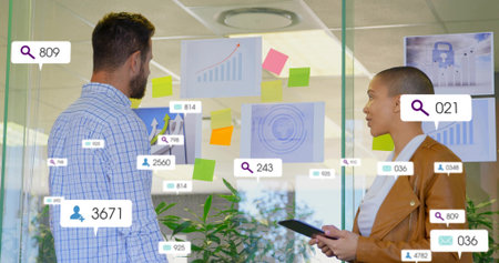 Standing two staff in suits studying glass charts at office, holding tablet, pointing at AR icons....