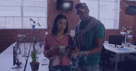 Showing smartphone, woman pink blouse holding mug while man in green tee viewing screens loft....