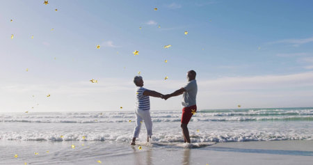 Holding couple leaning in shallow surf at beach, red shorts striped top, gold stars sparkling. Romance, seaside, coastline, horizon, sunshine, barefoot, togethernessの写真素材