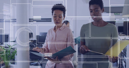 Reviewing paperwork, two coworkers in pink and green tops in office holding blue yellow folders. Collaboration, documents, openplan, monitors, modern, glass, digitalの写真素材