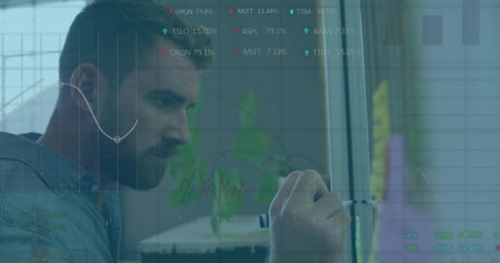 Writing senior male analyst in denim shirt on glass-board with marker at office, charts, copy space. Data, finance, stock, focus, overlays, analytics, dashboardの写真素材