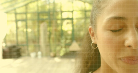 Closing eyes woman in right-side close-up greenhouse, hair pulled back, hoop earring, copy space. Portrait, serenity, calm, sunlight, plants, conservatory, glassの写真素材