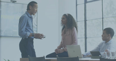 Presenting man in blue shirt holding remote while colleagues listening in room, with laptop screen. Meeting, team, boardroom, collaboration, business, modern, daylightの写真素材