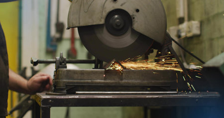 Cutting cutoff saw spinning blade in workshop, sending sparks while workpiece being clamped in vise. Abrasive, disc, metalwork, fabrication, industrial, shopfloor, guardの写真素材