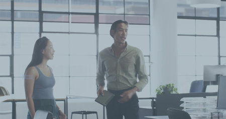 Discussing man wearing light shirt and dark pants holding tablet at open-plan office with monitors. Colleagues, collaboration, discussion, daylight, windows, workspace, modernの写真素材
