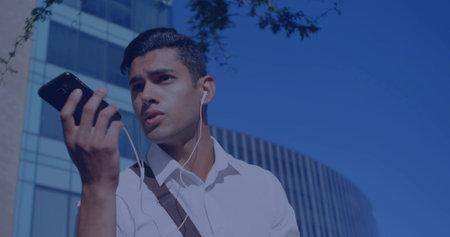 Speaking man wearing white shirt and shoulder bag in city, holding smartphone and wired earphones. Outdoor, professional, commute, mobile, wired, headphones, urbanの写真素材
