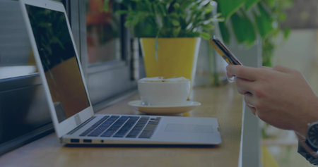 Using smartphone, man wearing dark-top and watch at window counter with laptop and cup, copy space. Cafe, bar, workspace, phone, coffee, plant, greeneryの写真素材