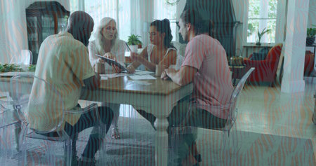 Discussing four adults in casual clothes reviewing paperwork at home dining area, with notebook. Group, collaboration, discussion, documents, notes, sunlit, daylightの写真素材