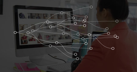 Reviewing woman in coral-blazer scrolling monitor thumbnails at desk with DSLR, nodes, copy space. Display, grid, camera, notebooks, workspace, editorial, creativeの写真素材