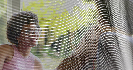 Smiling woman sleeveless pink top large glasses chatting through ripple glass at lounge, copy space. Panel, distortion, silhouette, window, greenery, dialogue, daylightの写真素材